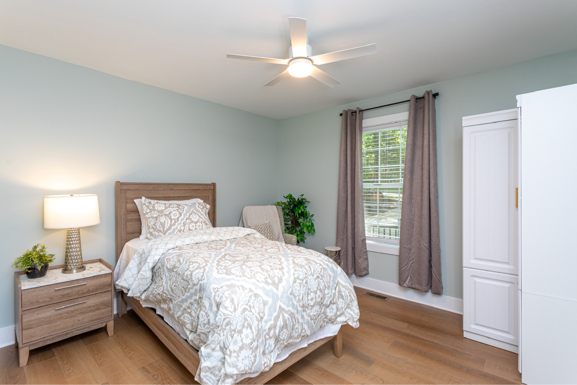 A private bedroom with warm-tone bedding, natural light, and a wardrobe